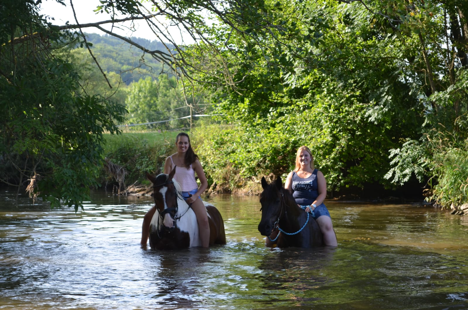 Zwei Mädchen reiten auf zwei Pferden durch einen Bach